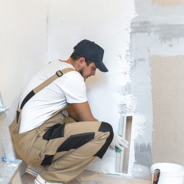Male painter with a putty knife in his hands makes repairs Male painter with a spatula in his hands makes repairs in home. Room renovation concept.